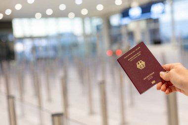 Havaalanı güvenlik noktasında uzun bir kuyruğun önünde pasaport tutan bir el. Gezginler modern bir terminalde güvenlik taraması için hazırlanıyorlar..