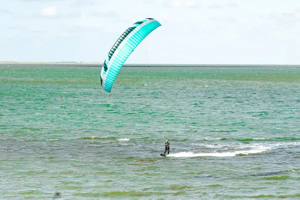 Uçurtma sörfçüsü ustalıkla havada süzülen canlı bir uçurtmayla ışıldayan turkuaz suyun üzerinde manevra yapar. Sahne güneşli bir öğleden sonrayı yakındaki heyecanla yakalıyor..