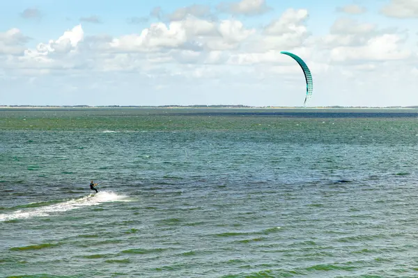 Yetenekli bir uçurtma sörfçüsü güneşli bir günde sakin sularda manevra yapar. Ufuk, üzerinde yumuşak dalgalar ve kabarık bulutlar bulunan bir kıyı zeminine sahiptir..