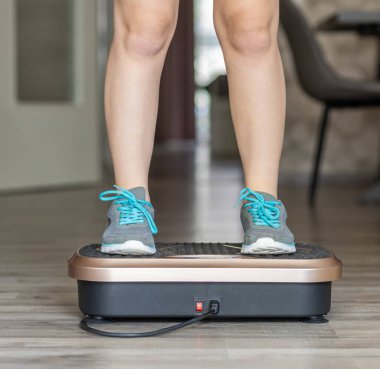 Şık bir ev ortamında titreşim plaka egzersiz makinesi kullanan kişi, fiziksel aktivite ve refah üzerine yoğunlaşarak, spor ve sağlığa önem verir.