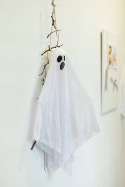 A spooky ghost decoration made with white fabric and twigs is hanging on a wall, adding a festive touch to the Halloween atmosphere in the room.
