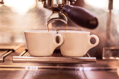 Kahve, hareketli bir kafedeki parlak bir espresso makinesinden iki beyaz espresso bardağına akıyor. Sabah enerjisini ve taze bira kokusunu yakalıyor..