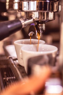 Rich espresso flows from an espresso machine into two white cups on a barista counter. The cafe has a warm atmosphere, ideal for coffee lovers enjoying their drinks.