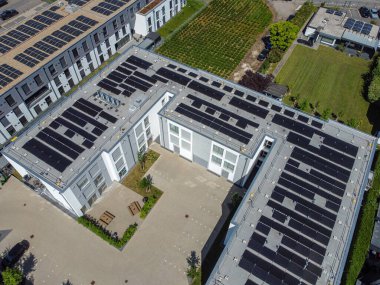 Çağdaş binaların düz çatılarına kurulmuş çoklu güneş panellerini gösteren hava görüntüsü.