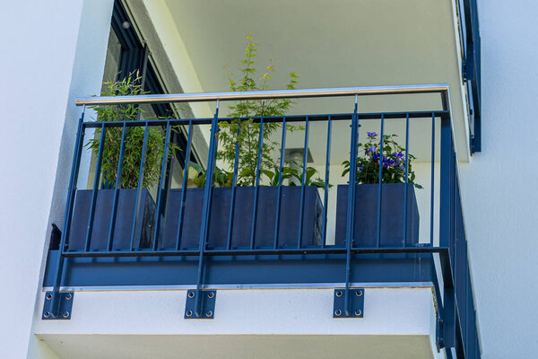 A balcony features two rectangular planters filled with lush green plants and colorful flowers. The modern design adds a refreshing touch to the building. Sunlight enhances the vibrant colors.