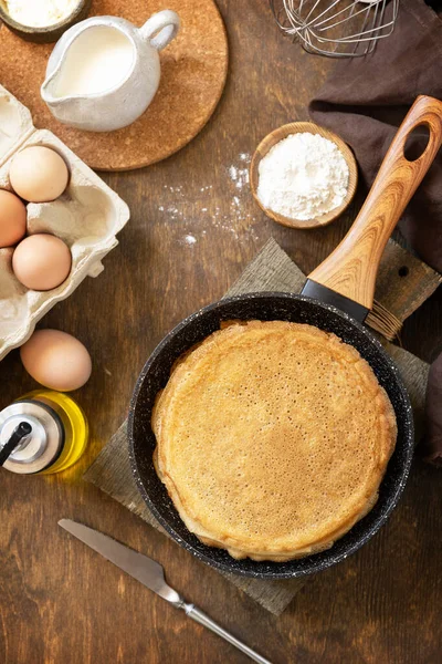 Celebrating Pancake day, cooking healthy breakfast. Delicious homemade crepes or pancakes in a frying pan and ingredients on a rustic table. View from above.