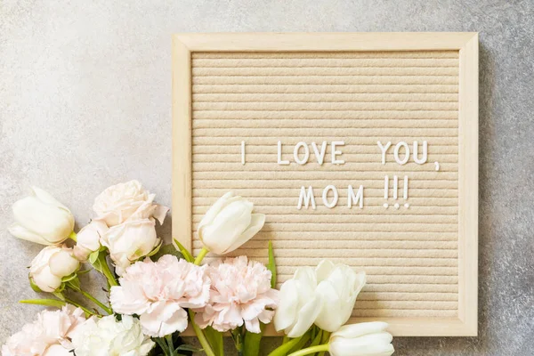 Happy Mother's Day. Letter I LOVE MOM on letterboard and beautiful spring flowers on light background. Womans day, wedding, mothers day greeting card. View from above.