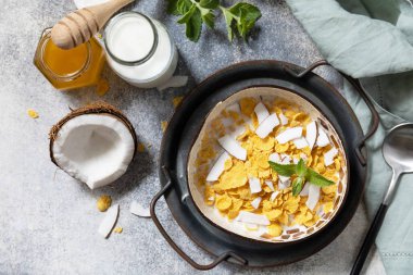 Yaz vejetaryen kahvaltısı. Mısır gevrekli kahvaltılık gevrek, hindistan cevizi içermeyen süt ve taş bir masanın üstünde taze hindistan cevizi dilimleri. Yukarıdan görüntüle. 