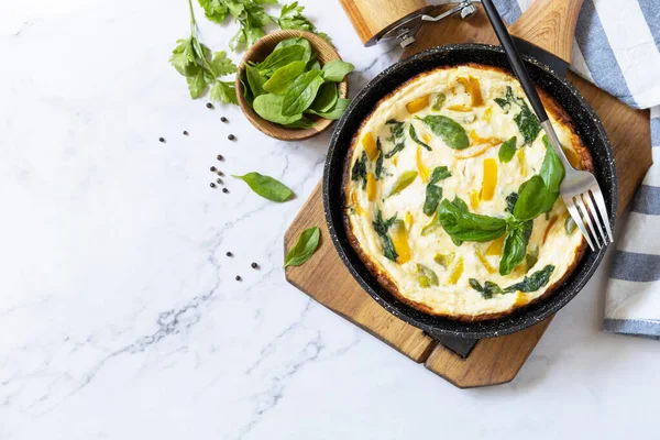 Spinach and cheese omelette. Frittata made of eggs, paprika and spinach in a frying pan on a marble countertop. View from above. Copy space.