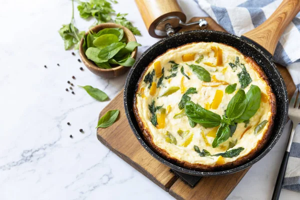Spinach and cheese omelette. Frittata made of eggs, paprika and spinach in a frying pan on a marble countertop. Copy space.