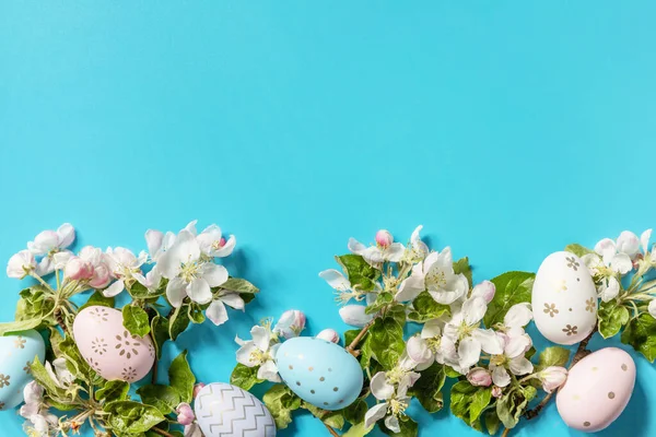 Easter composition with colorful eggs and flowers of apple tree on a blue background. Spring concept, flowers composition. Greeting card. View from above. Copy space.