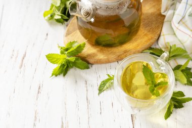 Bardak ve çaydanlık taze doğal bitki çayı ve kırsal ahşap masa üzerinde taze nane yaprakları. Organik aromaterapi gevşeme tıbbi sağlıklı içecek. Boşluğu kopyala. 