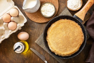 Celebrating Pancake day, cooking healthy breakfast. Delicious homemade crepes or pancakes in a frying pan and ingredients on a rustic table. View from above. 