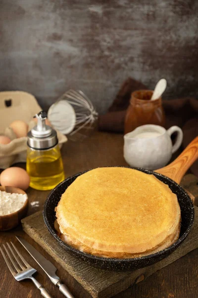 Celebrating Pancake day, cooking healthy breakfast. Delicious homemade crepes or pancakes in a frying pan and ingredients on a rustic table. Copy space.
