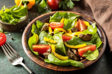 Warm salad from the baby spinach, chicken liver, tomatoes and peppers with spices and balsamic on stone background.