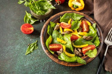 Warm salad from the baby spinach, chicken liver, tomatoes and peppers with spices and balsamic on stone background. Copy space.