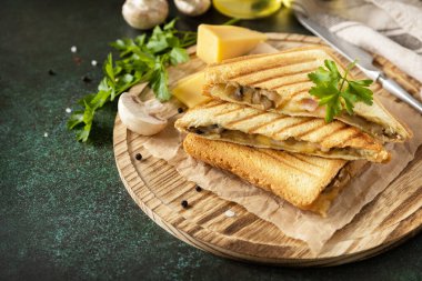 Izgara peynirli, pastırmalı ve mantarlı lezzetli sandviç. Koyu taştan bir masanın üstünde ev yapımı kahvaltı. Boşluğu kopyala. 
