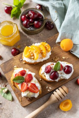 Vişneli sandviç, çilek, yumuşak peynir ve ballı taş zeminde ahşap tahta. Meyveli tost kahvaltısı, sağlıklı yemek..  