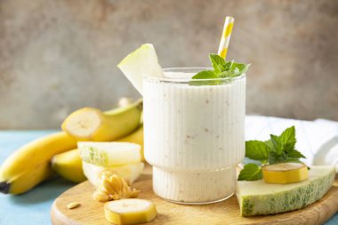 Taştan bir arka planda tahta tahtada kavun ve içecek bardağı olan muzlu smoothie. Detoks menüsü. Taze mevsimlik içecekler.