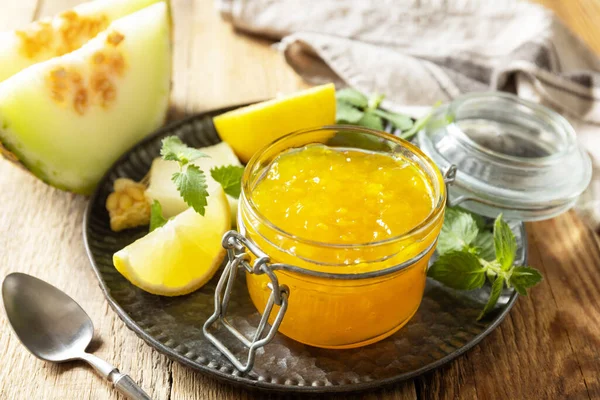 Sweet melon and citrus jam or jelly in small glass jar with fresh melon slices on wooden rustic table. Homemade preserve.