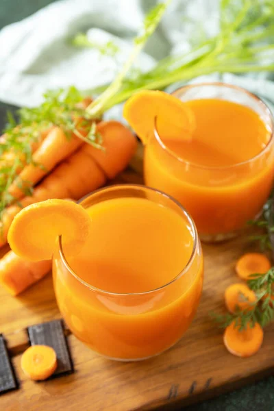 Carrot juice in a glass and fresh carrots with leaves on a stone table. Carrot healthy juice for detox. Healthy vegan vegetarian drink.