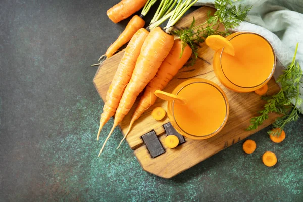 Carrot healthy juice for detox. Carrot juice in a glass and fresh carrots with leaves on a stone table. Healthy vegan vegetarian drink. View from above. Copy space.