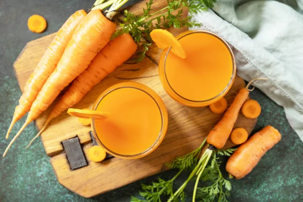 Carrot juice in a glass and fresh carrots with leaves on a stone table. Carrot healthy juice for detox. Healthy vegan vegetarian drink. View from above.