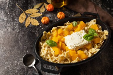 Balkabağından yapılmış Feta makarna tarifi, feta peyniri, sarımsak ve siyah taş zemin üzerinde otlar. Fetapasta. Fırında makarna, ya da Tiktok makarna. Boşluğu kopyala.  