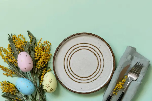 イースターエッグとミモザを背景にイースターディナーのテーブル設定 イースターの装飾コンセプト 上からの眺め コピースペース ストック画像