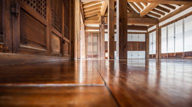 Namsangol Hanok Köyü 'nde, parke döşemeleri, ahşap kirişleri ve kafes kapıları olan geleneksel Kore iç mekanının alçak açılı görüntüsü. Kırsal mimari ve doğal malzemeler barışçıl bir atmosfer yaratır..