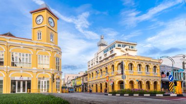 Phuket, Tayland - 11 Kasım 2024: Phuket Old Town 'daki tarihi Sino-Portekiz saat kulesi ve Kiralık Banka binası açık mavi gökyüzünün altından geçen kendine özgü mavi bir yerel otobüsle hareketli bir kavşak oluşturdu.