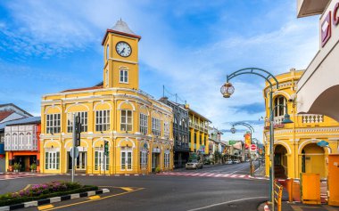 Phuket, Tayland - 11 Kasım 2024: Phuket Eski Kasabası 'ndaki ikonik Sino-Portekiz saat kulesi parlak mavi gökyüzü altında renkli koloni tarzı binalarla çevrili canlı bir kavşakta duruyor.