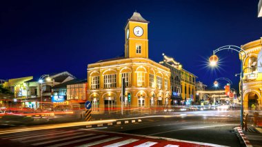 Phuket, Tayland, 9 Kasım 2024: Phuket Eski Şehir Saat Kulesi 'nin canlı sarı ışıklarla aydınlatılmış, hareketli trafik ışığı yolları ve kültürel sokak dekorasyonlarıyla dolu gece manzarası.