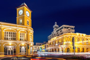 Phuket, Tayland, 9 Kasım 2024: Phuket Eski Şehir Saat Kulesi 'nin canlı sarı ışıklarla aydınlatılmış, hareketli trafik ışığı yolları ve kültürel sokak dekorasyonlarıyla dolu gece manzarası.