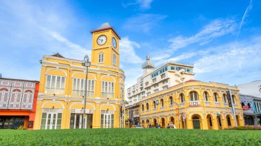 Phuket, Tayland - 10 Kasım 2024: Phuket Old Town 'daki Sino-Portekiz sarı saat kulesi ve Chartered Bank binası, yemyeşil yemyeşil, canlı mavi gökyüzü altında,