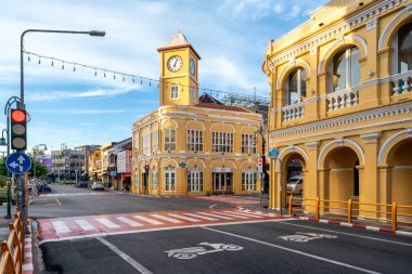 Phuket, Tayland - 10 Kasım 2024: İkonik sarı saat kulesi Phuket Eski Kasabası 'nda sakin bir kavşakta duruyor, açık mavi gökyüzü altında Çin-Portekiz mimarisini sergiliyor.