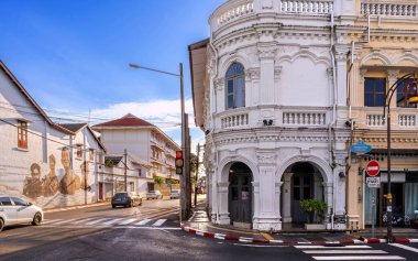Phuket, Tayland - 11 Kasım 2024: Phuket Eski Kasabası 'ndaki tarihi beyaz bir Sino-Portekiz binası, güneşli bir günde, kültürel mirası yansıtan duvar resmi dekore edilmiş bir sokak köşesinin yanında duruyor..