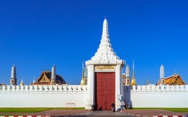 Bangkok, Tayland-30 Aralık 2024: Bangkok Büyük Sarayı 'nın Svasti Sopha Kapısı, mavi gökyüzü altında beyaz duvarlar ve altın kuleler yer alıyor. Yakındaki turistler de olaya canlılık katıyor..