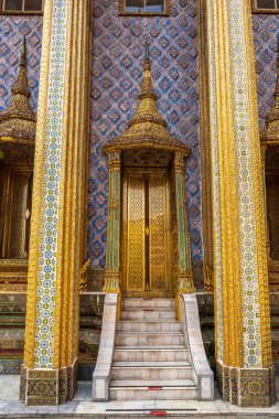 Tayland, Bangkok 'ta ünlü bir tapınak olan Wat Phra Kaew' da geleneksel Tayland mimari tarzında süslü sütunları ve merdivenleri olan renkli altın tapınak girişi.