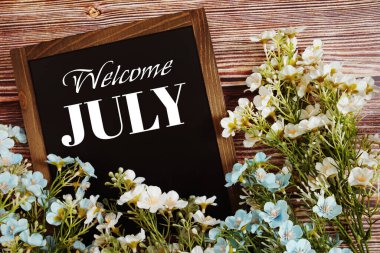 Tahta arka planda çiçek desenli Temmuz mesajına hoş geldiniz.