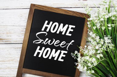 Ahşap arka planda çiçek süslemesi olan evim güzel evim mesajım.