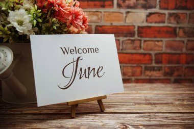 Welcome June text with flower bouquet decoration on wooden and old brick wall background