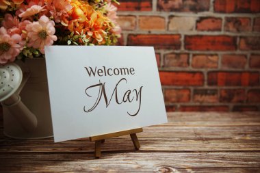 Welcome May text with flower bouquet decoration on wooden and old brick wall background