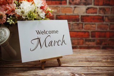 Welcome March text with flower bouquet decoration on wooden and old brick wall background