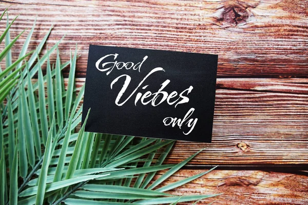 Good vibes only text message top view on wooden background with green leaf decoration