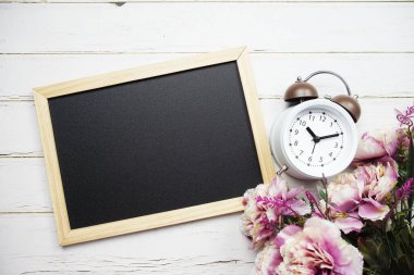 Çiçek buketli boş tebeşir tahtası ve ahşap arka planda çalar saat.