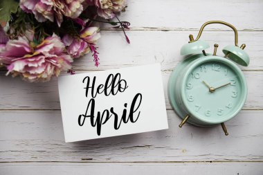 Hello April text message with alarm clock top view on wooden background clipart