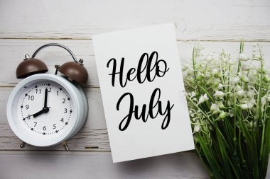 Merhaba, çiçekli Temmuz mesajı ve ahşap zemin üzerindeki çalar saat.