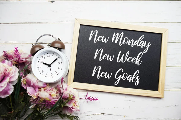New Monday, New Week, New Goals text message with alarm clcok and flower decoration on wooden background