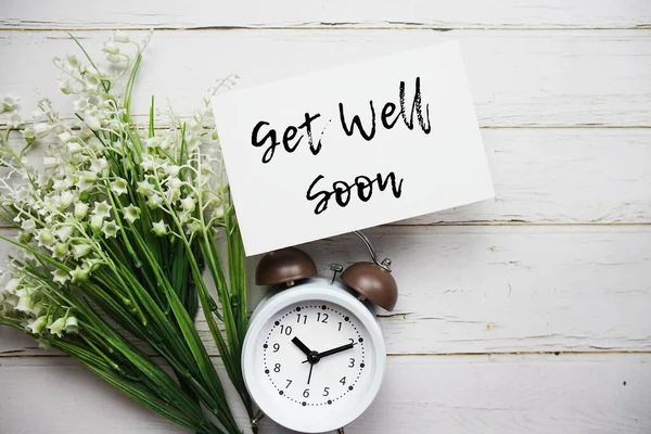 Get well Soon text message with alarm clock top view on wooden background